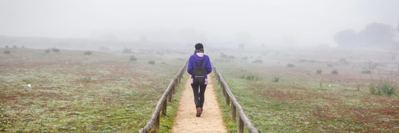 woman walking alone on a field surrounded by fog.