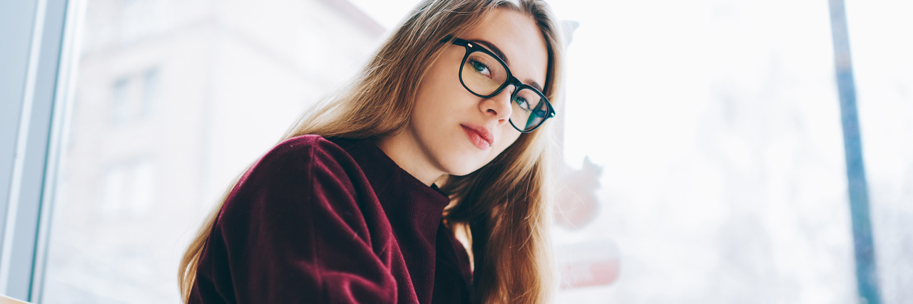 woman with glasses and long hair in a purple sweater looking seriously at camera at a coffee shop