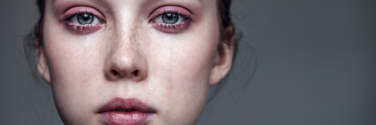 How Being Poor Makes My Mental Health Worse up close photo of a woman crying with tears streaming down her face and a straight face