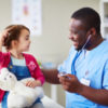 Happy male doctor communicating with child in clinic