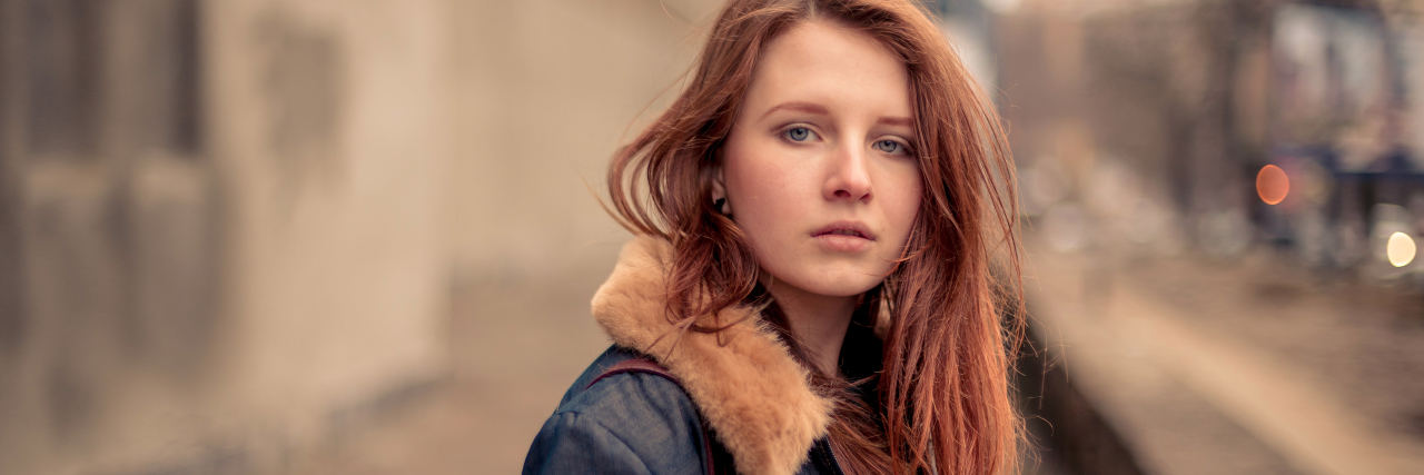 How My OCD Presented Itself Growing Up young red-haired woman in jean jacket with purse looking at camera seriously