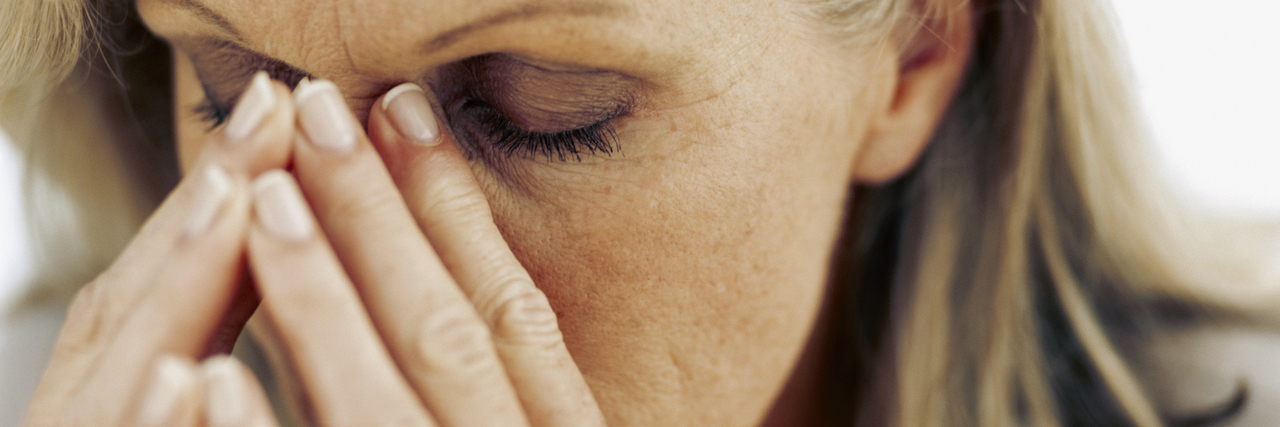 What Good Days and Bad Days Are Like With Parkinson's Disease A close up of a woman with silver hair resting her head in her hands and closing her eyes