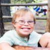 Cute little boy with Down syndrome sitting at a picnic table.