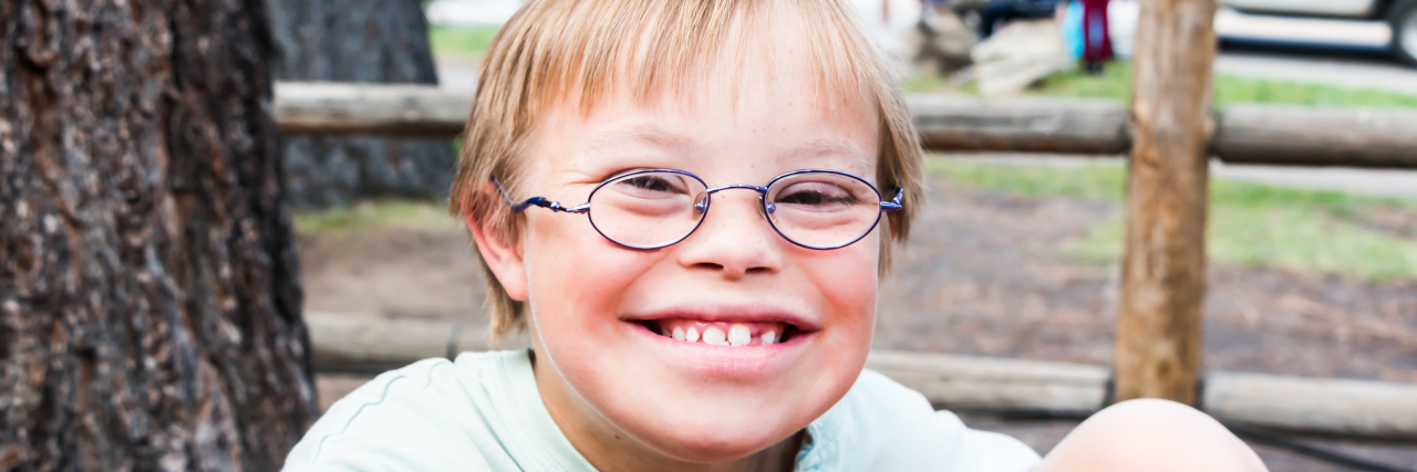 There's Nothing Wrong With Having Down Syndrome Cute little boy with Down syndrome sitting at a picnic table.
