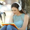 Woman wearing headphones and reading outdoors.