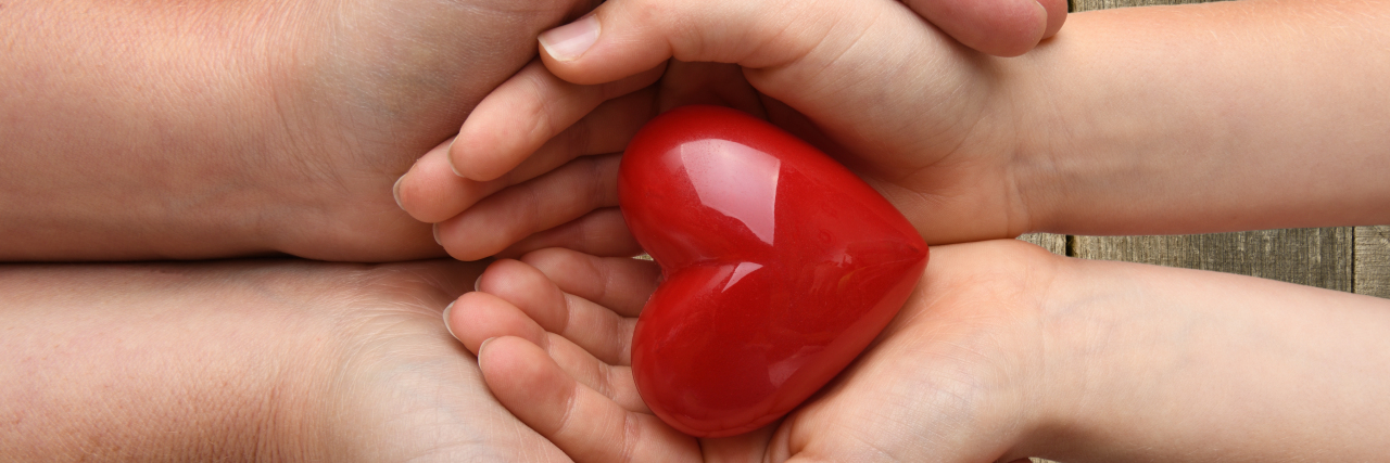 an adult and child's hands holding a red heart