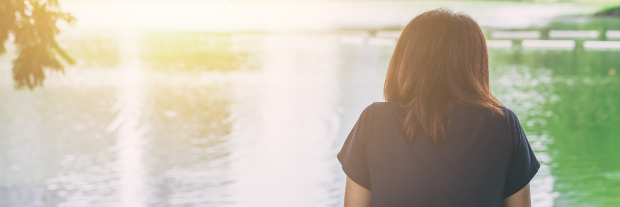 Why Wait Times Make Getting Treatment for Mental Illness Hard woman in a navy shirt and white shorts sitting on the edge of a dock looking out into the water
