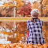 Woman sitting near a lake in fall season surrounded by colorful leaves