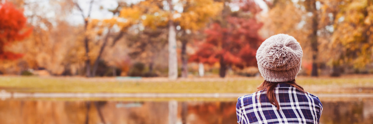 The Difficulty Navigating October as a Breast Cancer Survivor Woman sitting near a lake in fall season surrounded by colorful leaves