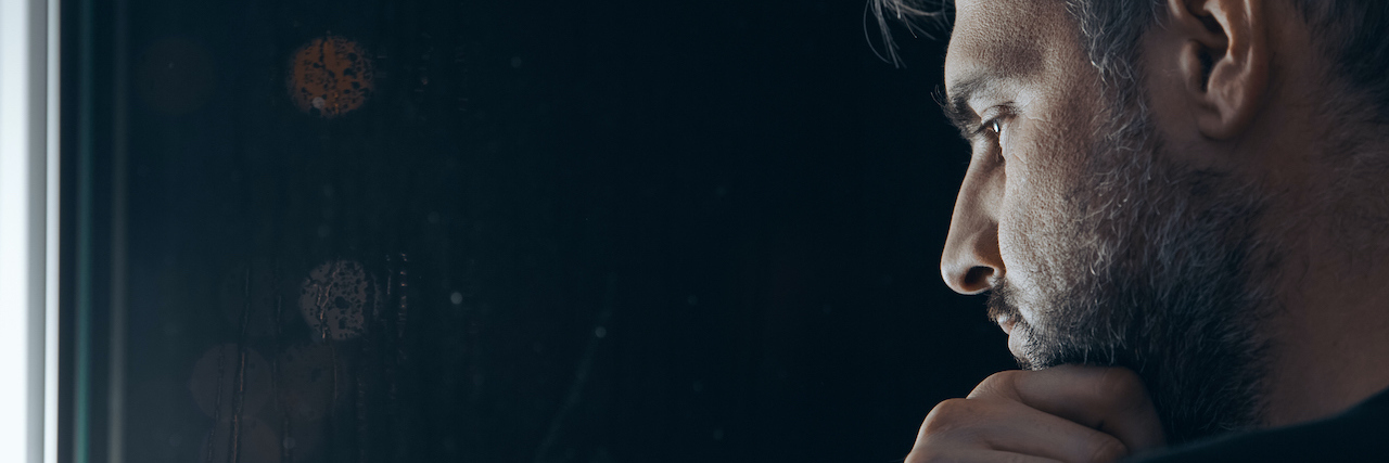 Parkinson's: What to Know When People Stare Man with beard holding his chin, standing beside a window at night