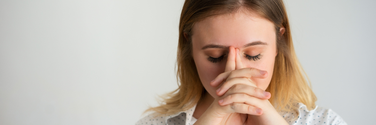 Why I Can't 'Win' at Time Management With Anxiety woman with shoulder-length brown hair in a white blouse with her eyes closed and hands together in front of her face