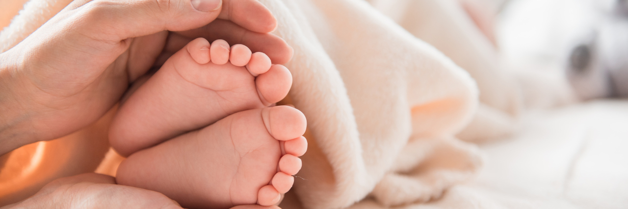 What It's Like Being a New Mom With Endometriosis close up of woman's hands holding baby feet