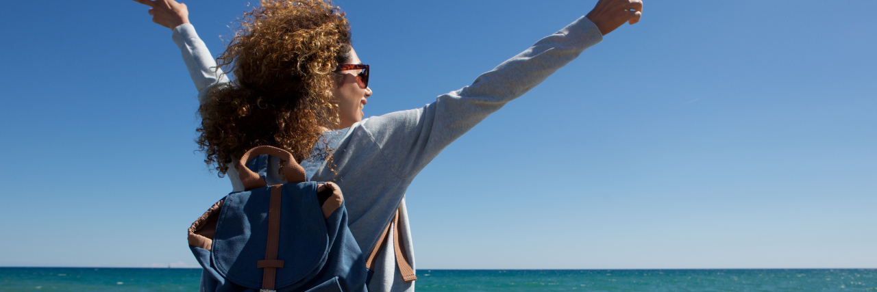 Schizoaffective Disorder Took Over My Life Until I Got Help woman sitting on a rock over the ocean with her arms stretched out