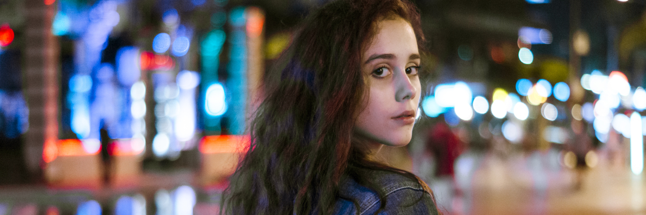 A woman looks back over her shoulder in front of the lights of the city.