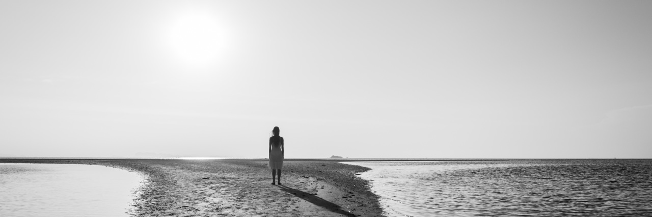 Silhouette of woman standing alone on small sand island.