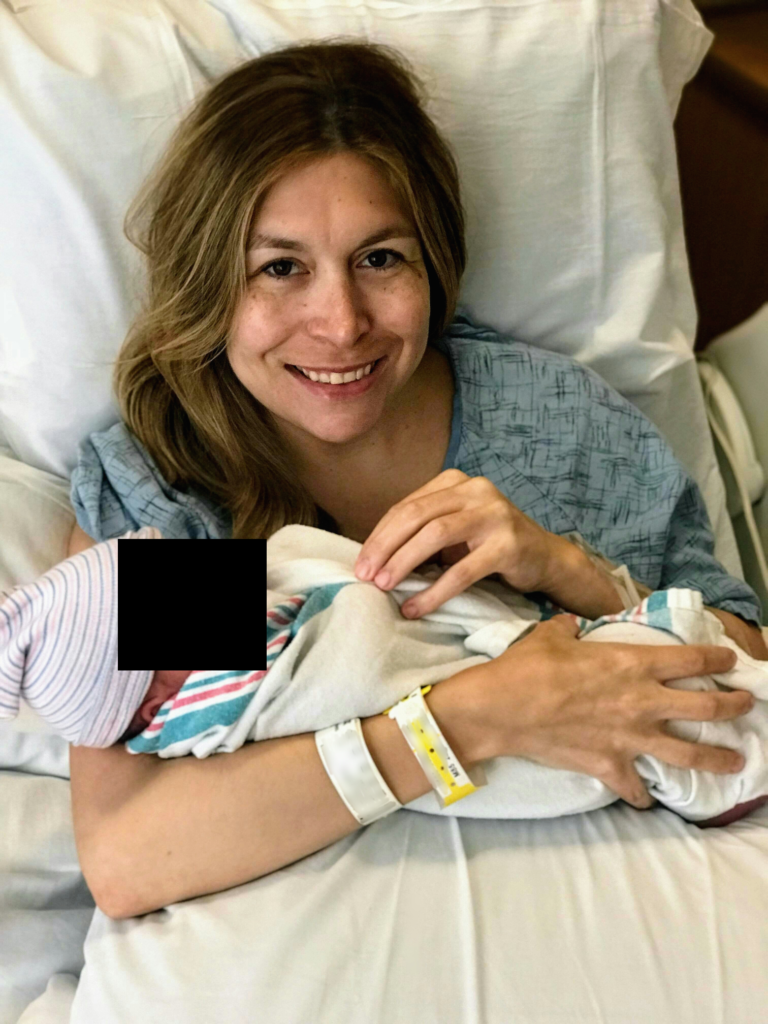 photo of mother holding newborn baby in hospital bed, smiling for camera