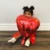 A little girl sitting on floor and holding a red balloon
