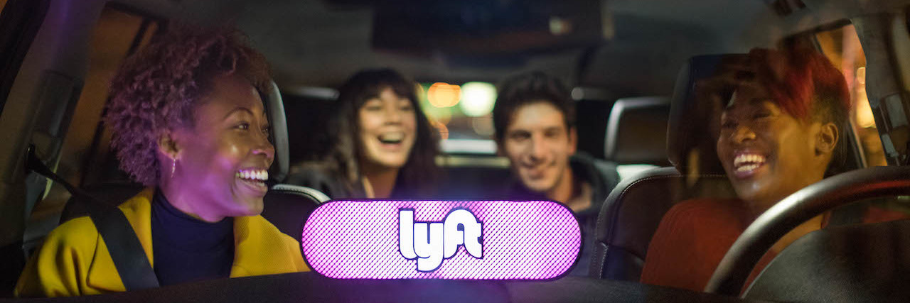Four people in a car with lighted Lyft sign on the dashboard