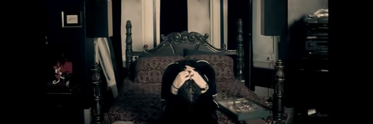 Heavy Metal Songs About Dealing With Depression screenshot of video for Korn song Alone I Break, showing lead singer with head in hands sitting on bed alone