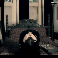 screenshot of video for Korn song Alone I Break, showing lead singer with head in hands sitting on bed alone