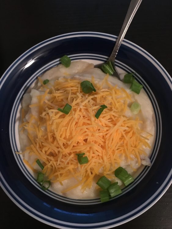 Bowl of potato soup topped with shredded cheddar cheese and diced scallions.