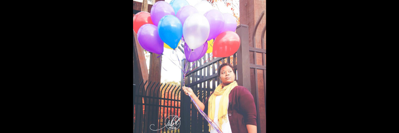 A woman stands holding balloons in front of a camera.