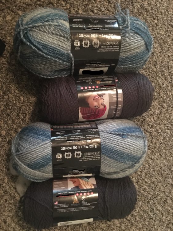 Four spools of yarn in alternating light and dark shades of grey, on a grey carpet.