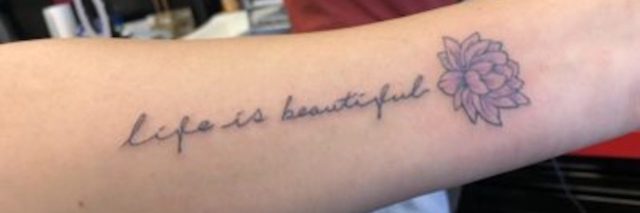 Photo of author's tatoo. Cursive writing of "life is beautiful" on her arm with a lotus flower next to it