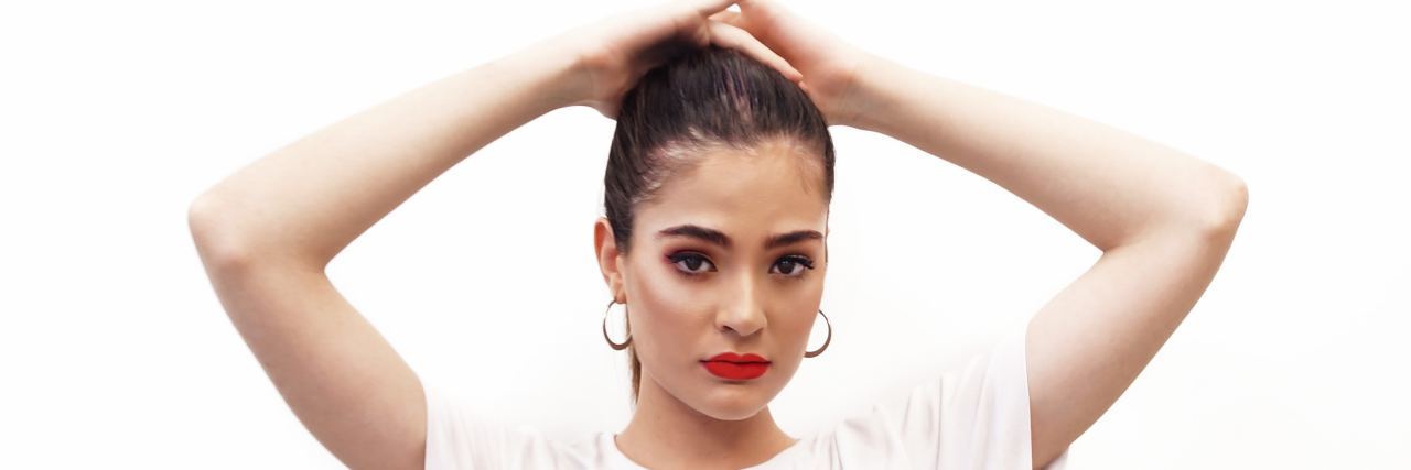 How I Used My 'Resting Bitch Face' to Hide My Anxiety woman in a white shirt and striped pants with her hands on her head looking seriously into the camera with red lipstick