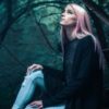 photo of woman with pink hair sitting in woods and looking up