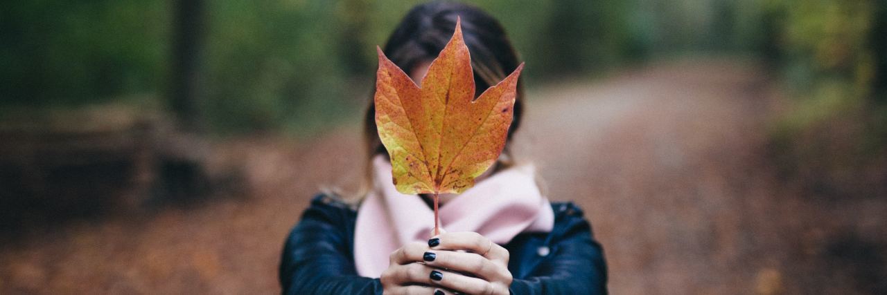 photo of woman holding up autumn fall leaf covering her face