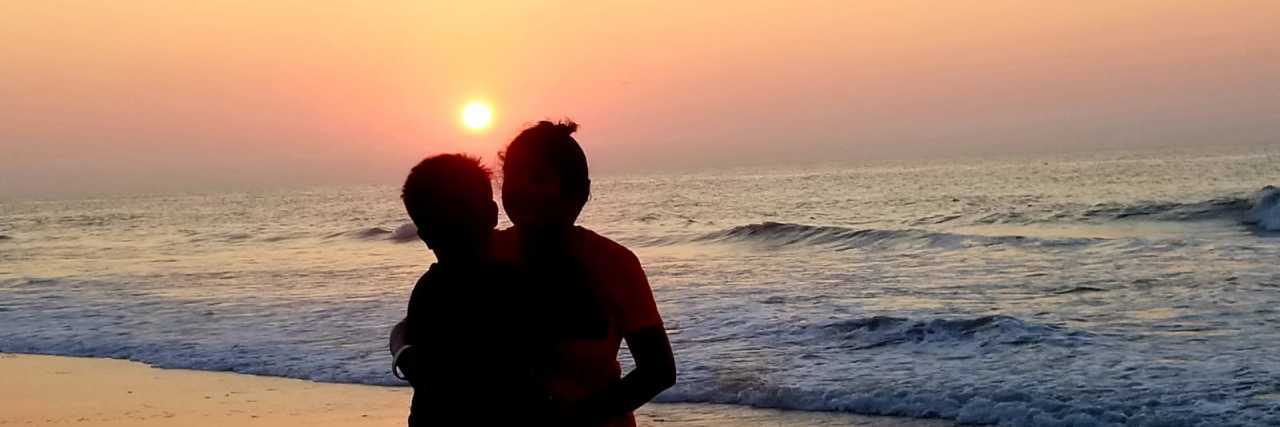 Tulika holding her son on the beach at sunset.