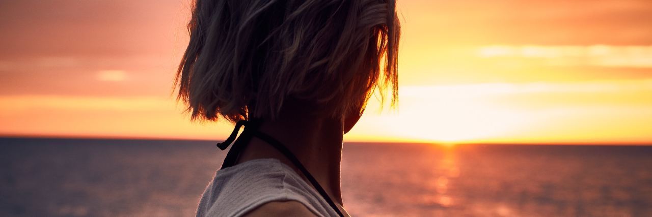 photo of woman silhouetted against sunset over ocean