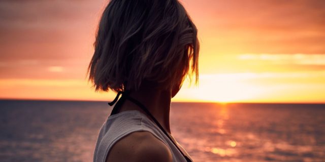 photo of woman silhouetted against sunset over ocean
