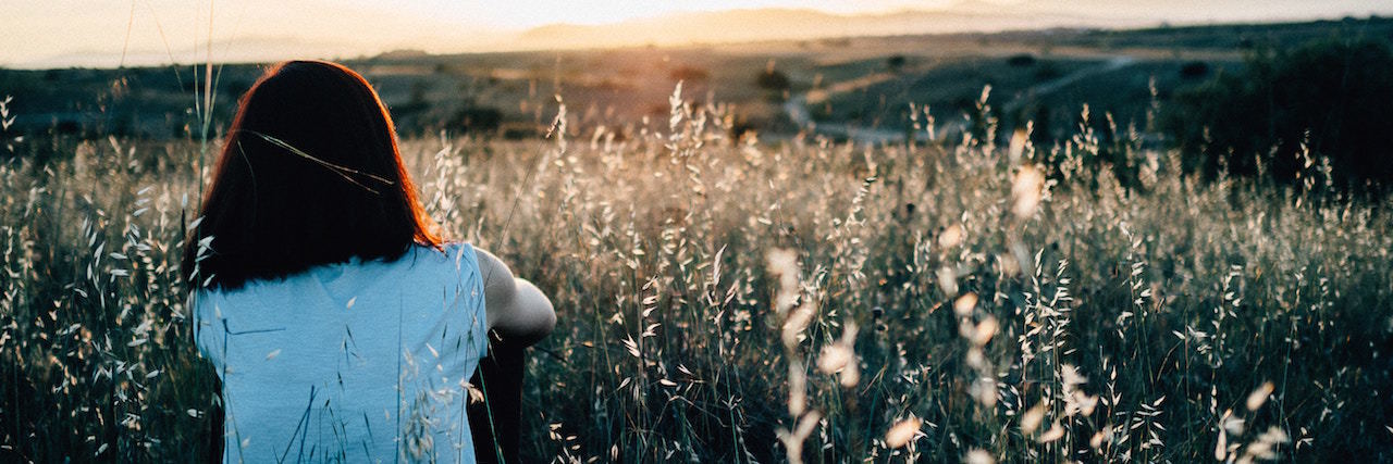 Saying Goodbye to Toxic Friendships A woman sitting in a field and watching at the sunset