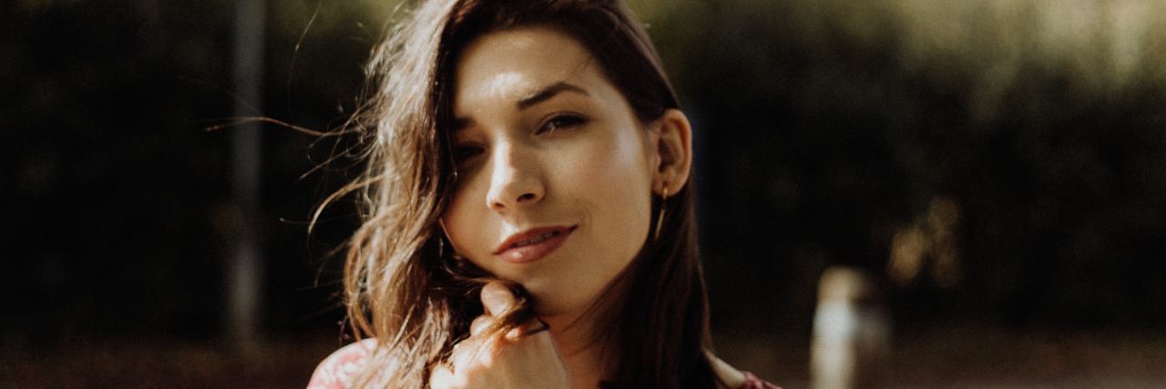 Traits That Prove Borderline Personality Disorder Stigma Is Wrong photo of young woman smiling for the camera with hand raised to her chin