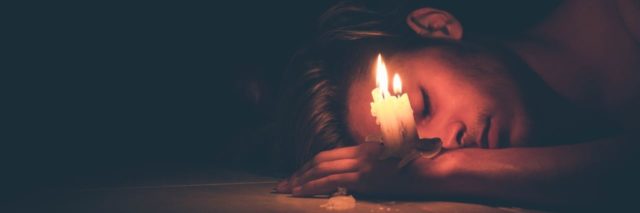 photo of man lying on floor in darkness with candle balanced on his hand
