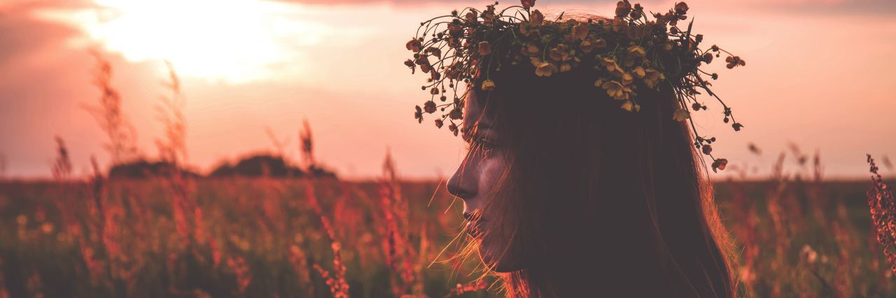 When People Invalidate My Bipolar Disorder Because of My Optimism Woman with brown hair and a crown of sunflowers on her head looking to the left in a field of flowers