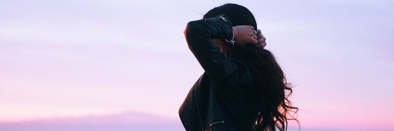 Please Listen to Me Before You Call the Cops About My Suicidal Thoughts woman with wavy brown hair standing to the side in the sunset with her hands behind her head grabbing her hair