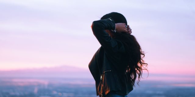Please Listen to Me Before You Call the Cops About My Suicidal Thoughts woman with wavy brown hair standing to the side in the sunset with her hands behind her head grabbing her hair