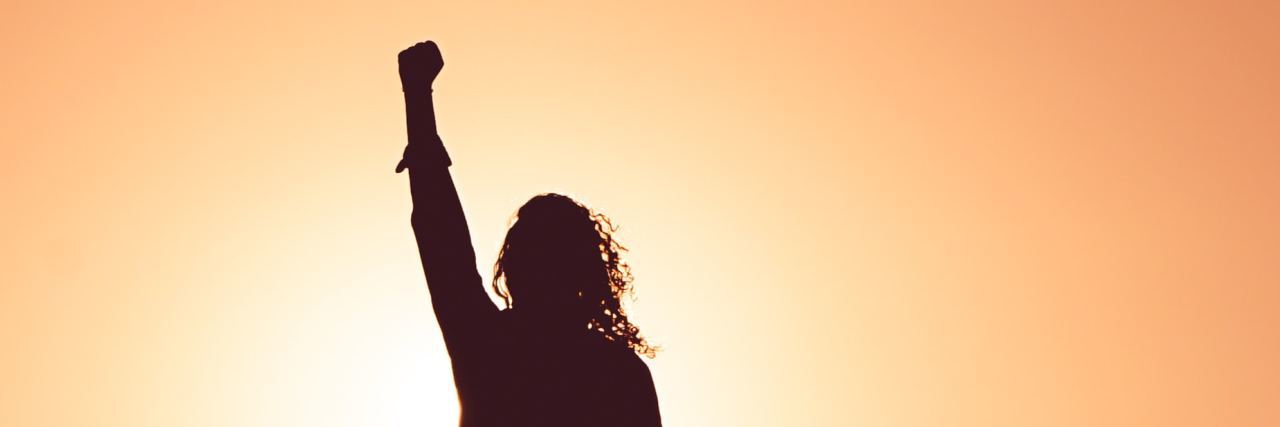 photo of woman silhouetted against sunset with fist raised into air