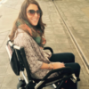 Nicole smiling, sitting outdoors in her portable wheelchair.