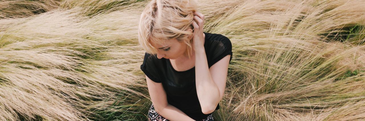What to Know About Opening Up About a Mental Illness photo of blonde woman sitting in field of long grass looking away with hand in hair