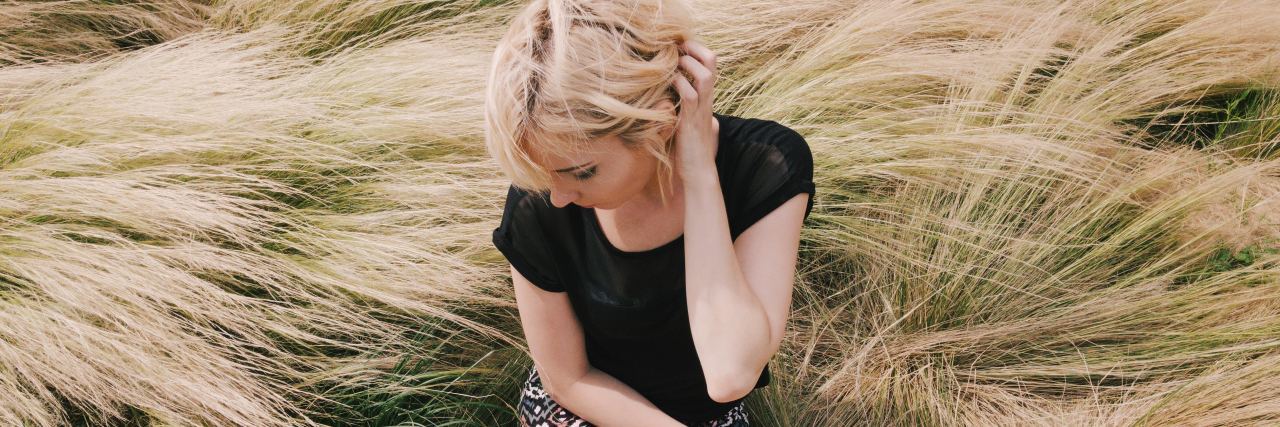 photo of blonde woman sitting in field of long grass looking away with hand in hair