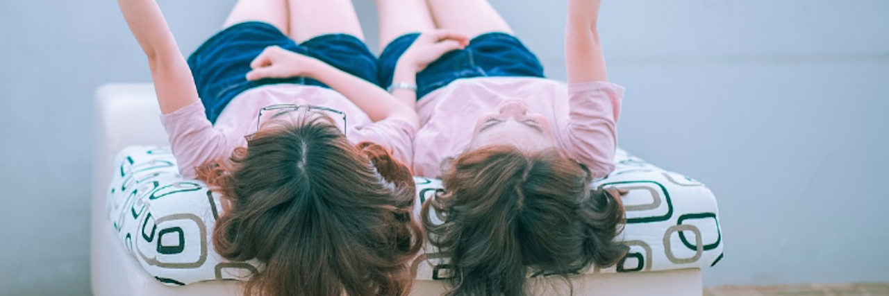 What It's Like to Have a Sibling With Trigeminal Neuralgia two women dressed in identical clothing, laying down