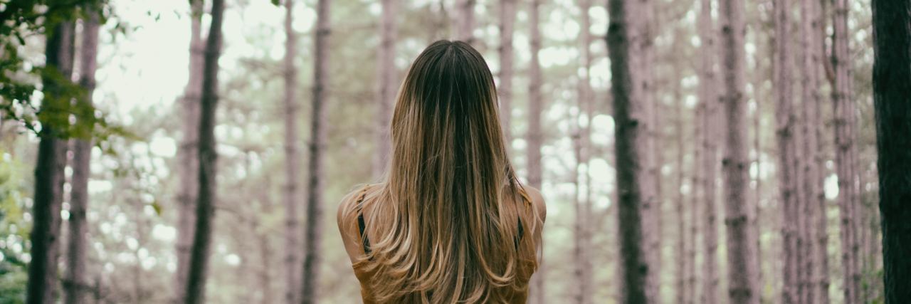 My Trauma Therapist Is Retiring and I'm Struggling With It photo of woman standing in forest looking at trees