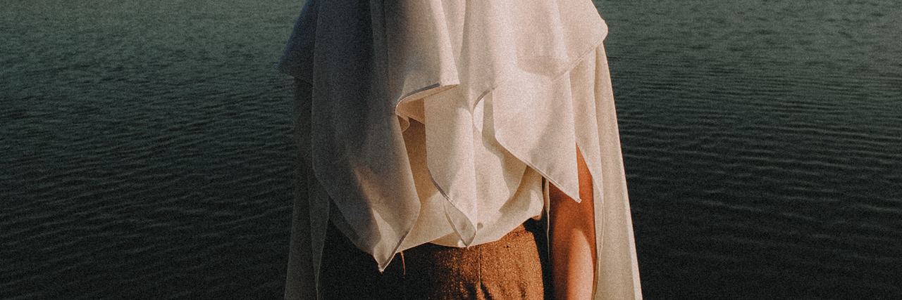 photo of person standing in front of lake with sheet covering head and upper arms