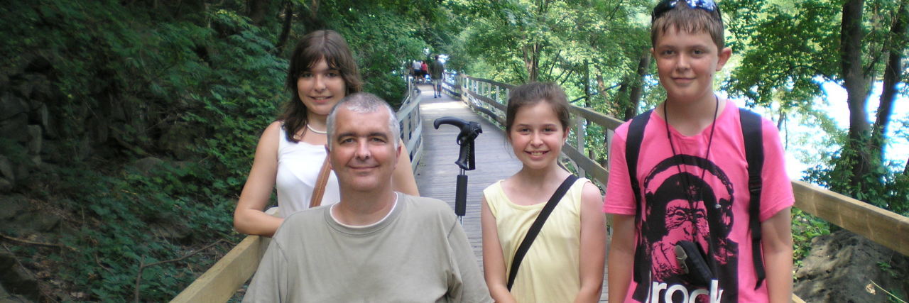 How Chronic Illness Affects Families: The We Diagnosis Suzanne's family on a wooden bridge. Her father is sitting in his wheelchair.