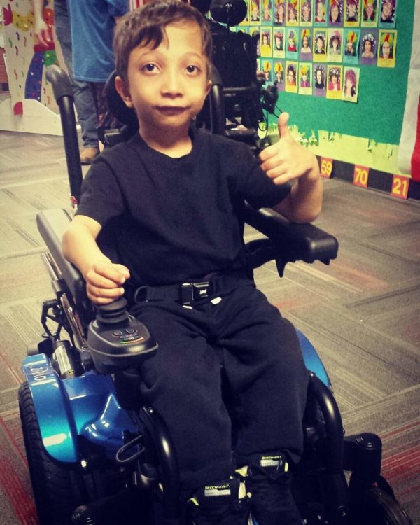 the author's son in his wheelchair, giving a thumbs up