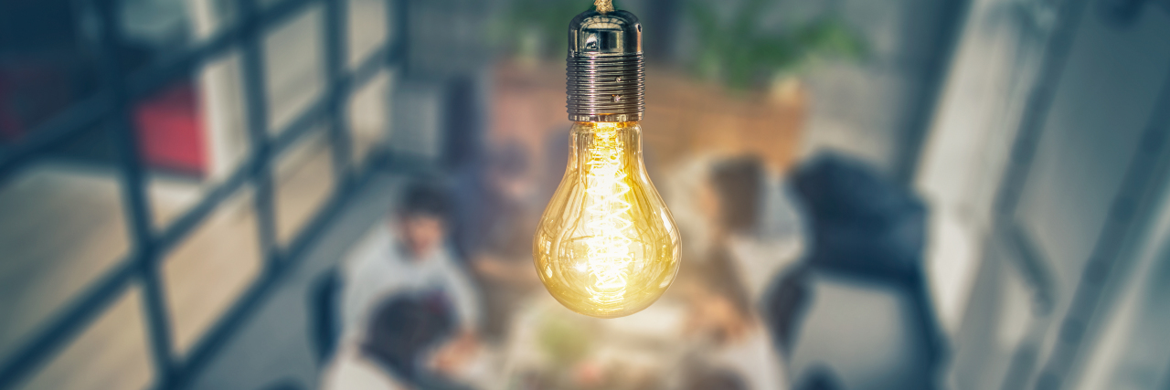 a lightbulb lit up in front of a table of people working together